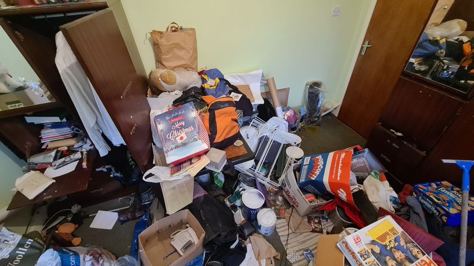 Cluttered room with wardrobe, boxes and bags before a house clearance in Sutton