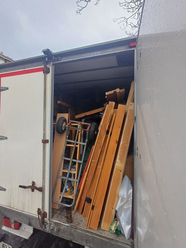 Box van rear doors open, loaded with timber, a sack truck and furniture panels from a clearance