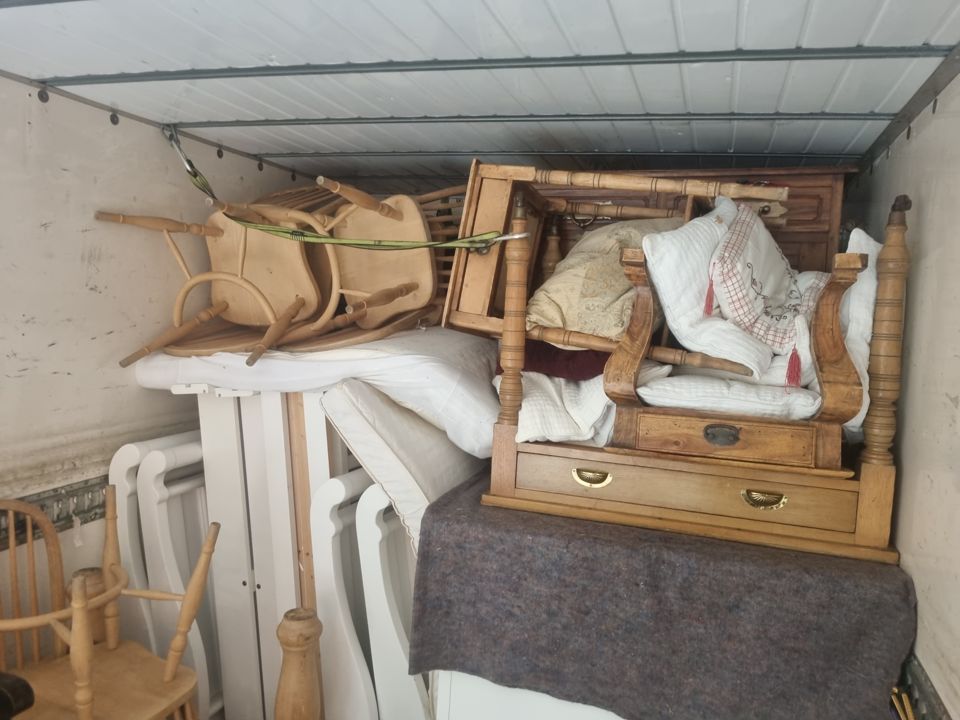 Box van interior loaded and strapped with pine chairs, bed frames, mattresses and a chest